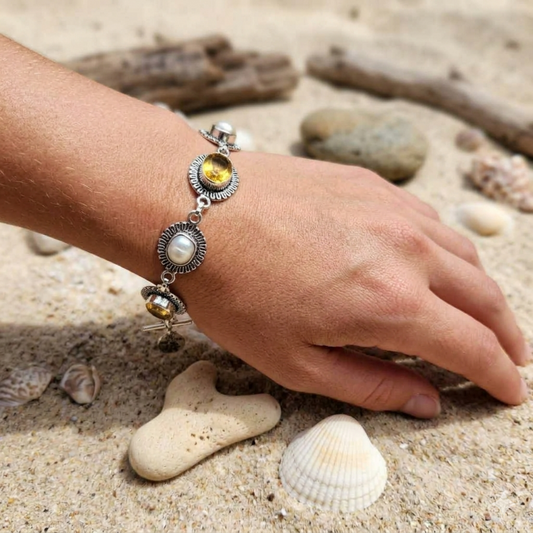Hand wearing a silver bracelet with gemstones on a sandy background