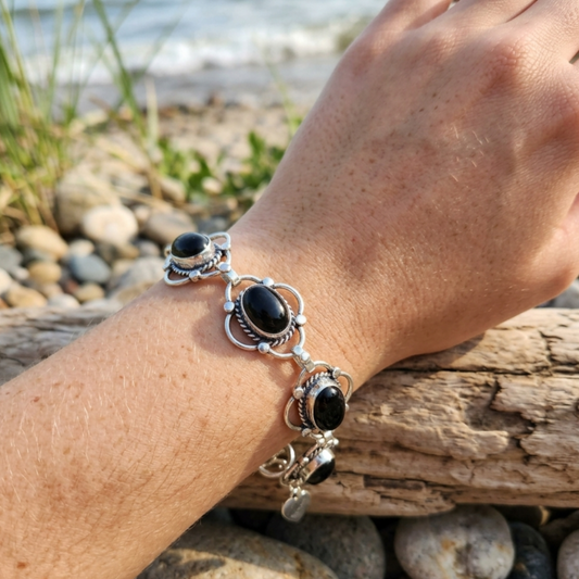 Hand wearing a silver bracelet with black stones on a beach.