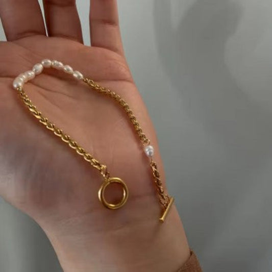 Gold chain necklace with a small round pendant held in a hand against a neutral background