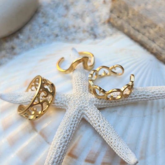 A set of three rose gold bohemian toe rings placed on a white textured surface with a shell, showcasing their waterproof and tarnish-resistant properties.
