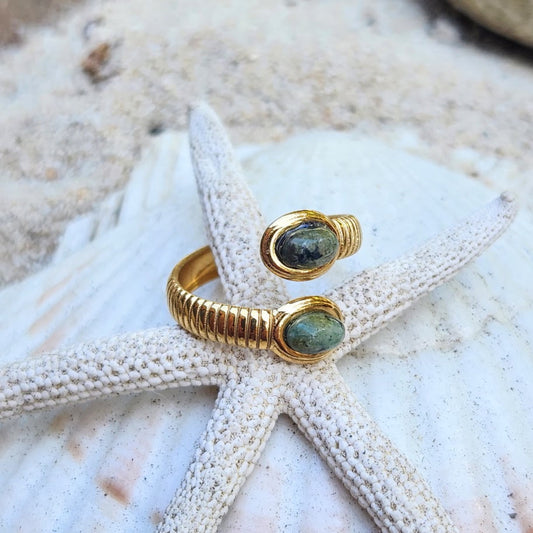 An 18k gold ring with double turquoise stones, displayed on a white starfish with a sandy background.