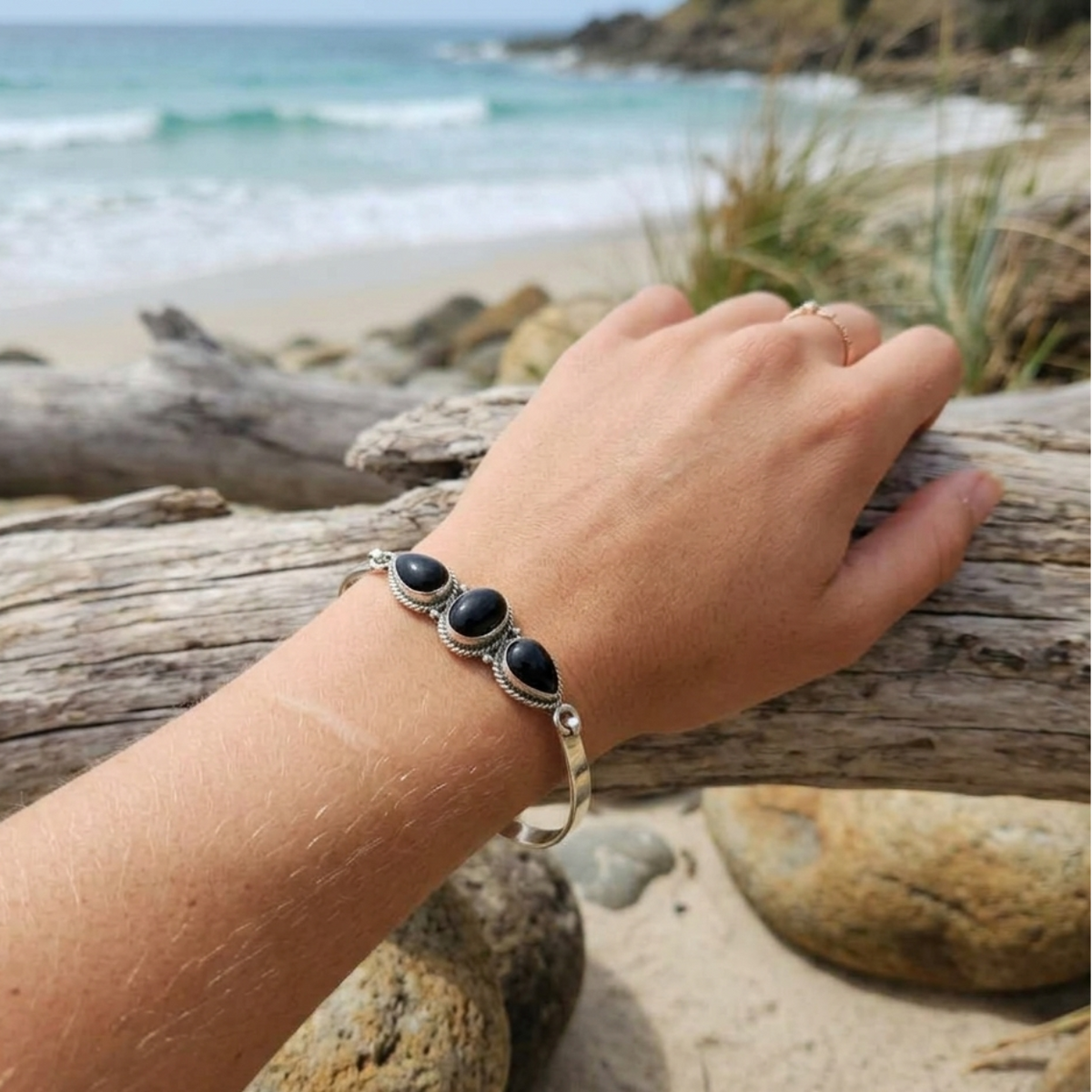 Hand wearing a silver bracelet with black stones on a beach.