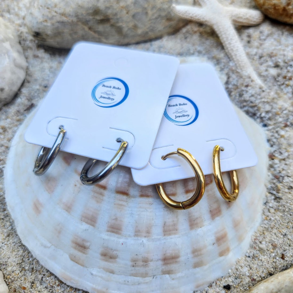 Gold hoop earrings on white cards with 'Beach Babe Jewelry' label, placed on a shell.