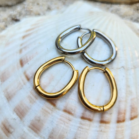 Three hoop earrings in gold and silver on a seashell.