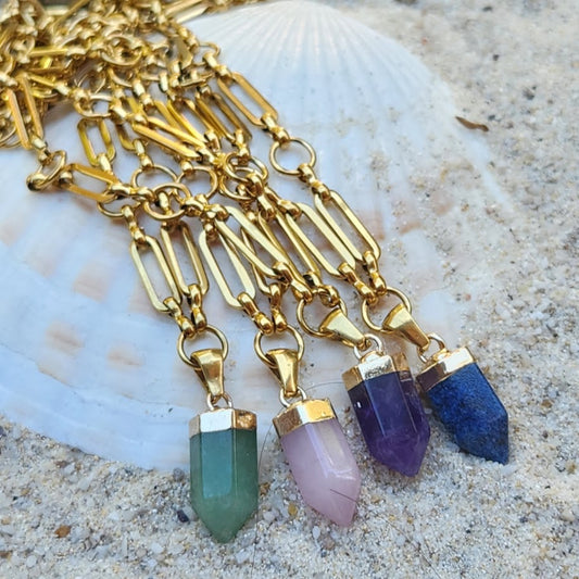 Gold necklaces with colorful pendant drops on a sandy background