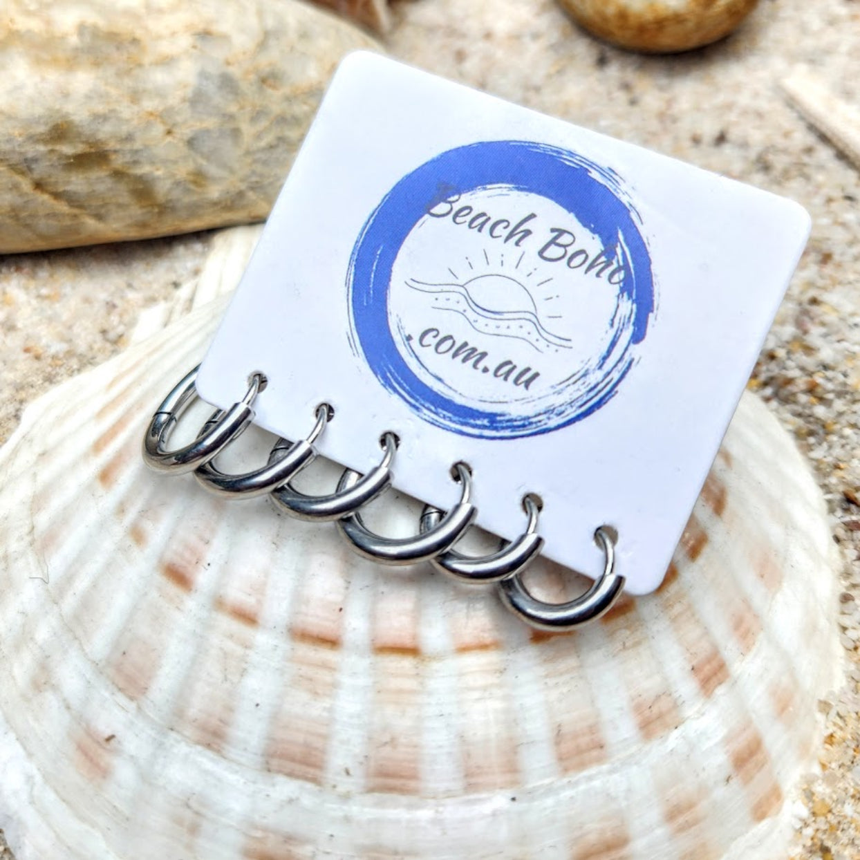 Set of silver keychains on a white card with 'Beach Boho' branding, placed on a shell.