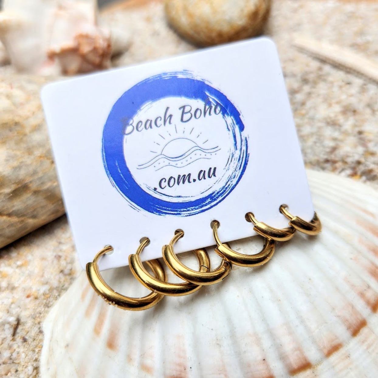 Gold hoop earrings on a card with 'Beach Boho' branding, placed on a shell.