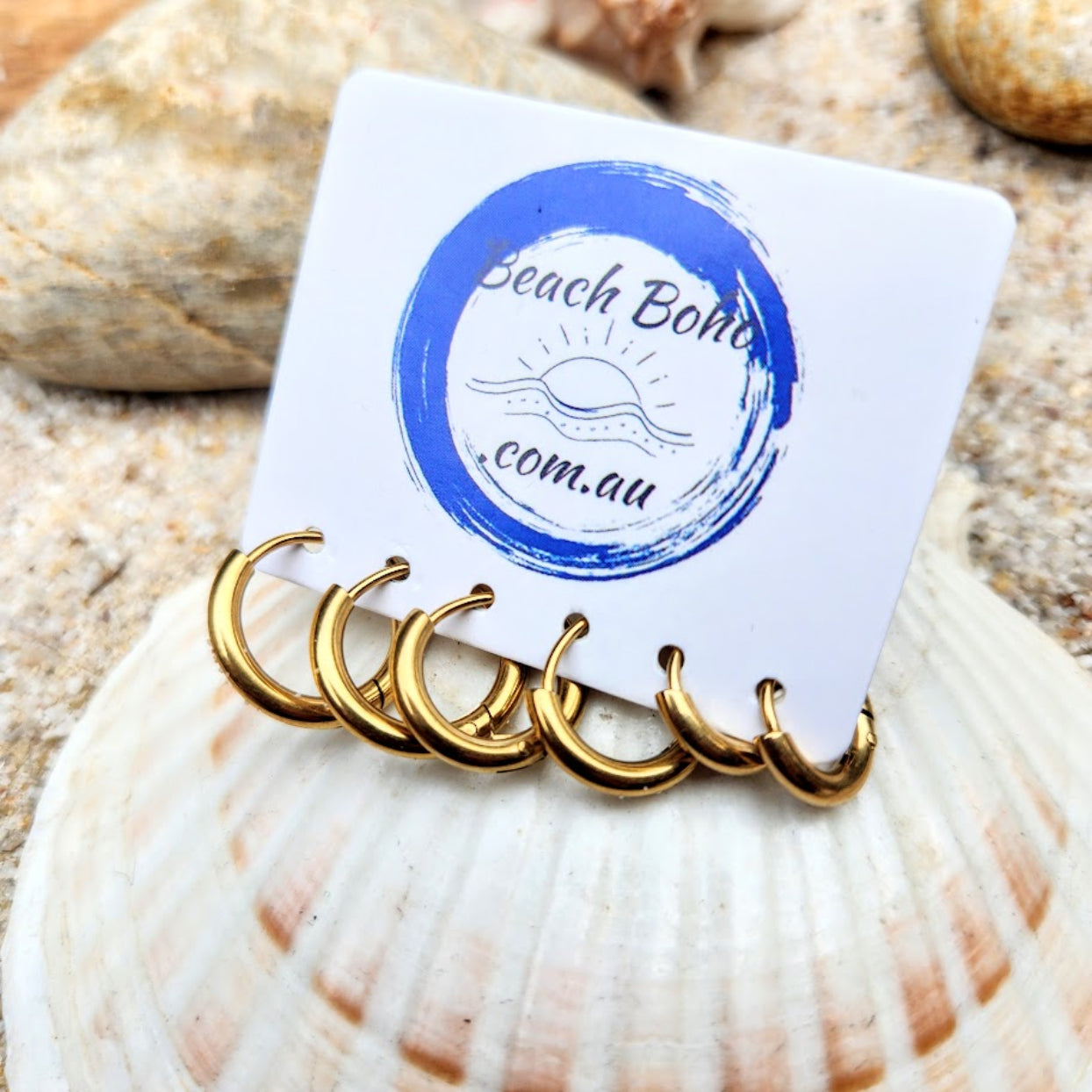 Set of gold earrings on a card with 'Beach Boho' branding, placed on a shell.