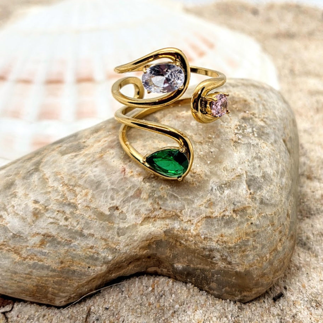Gold ring with green and purple gemstones on a stone surface