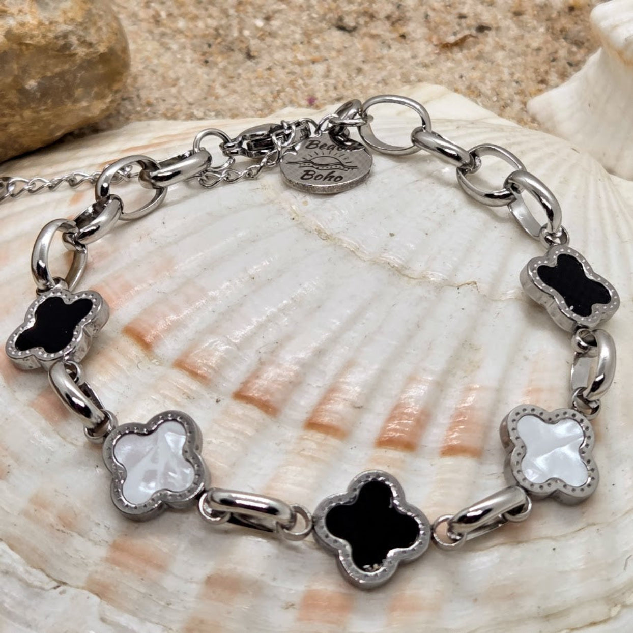 Silver bracelet with black and white clover-shaped charms on a seashell background
