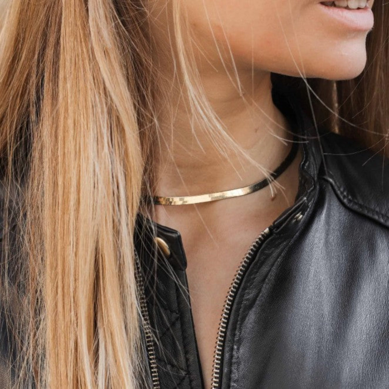 Close-up of a person wearing a black leather jacket and gold necklace.
