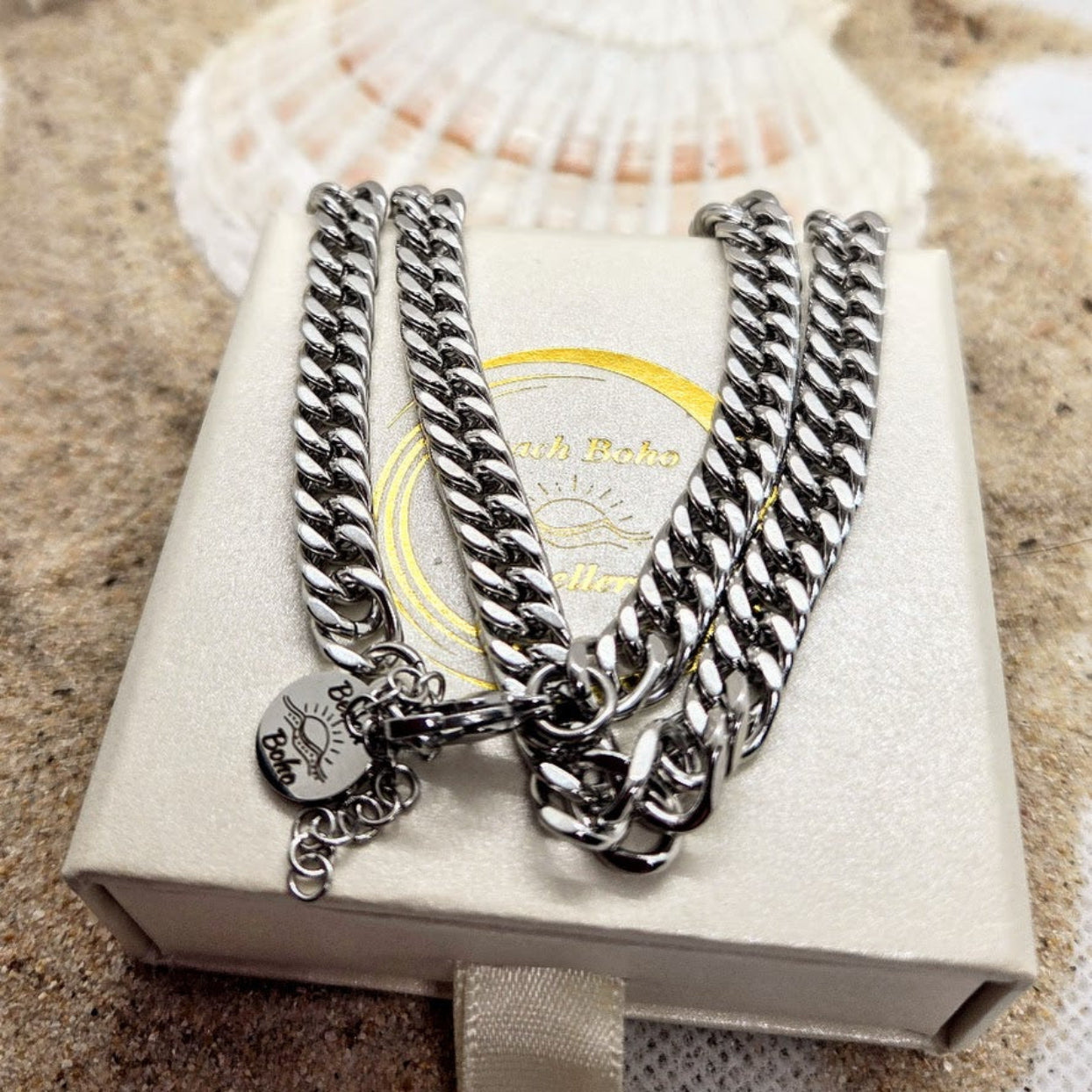 Silver chain bracelets with charms on a branded box against a textured surface