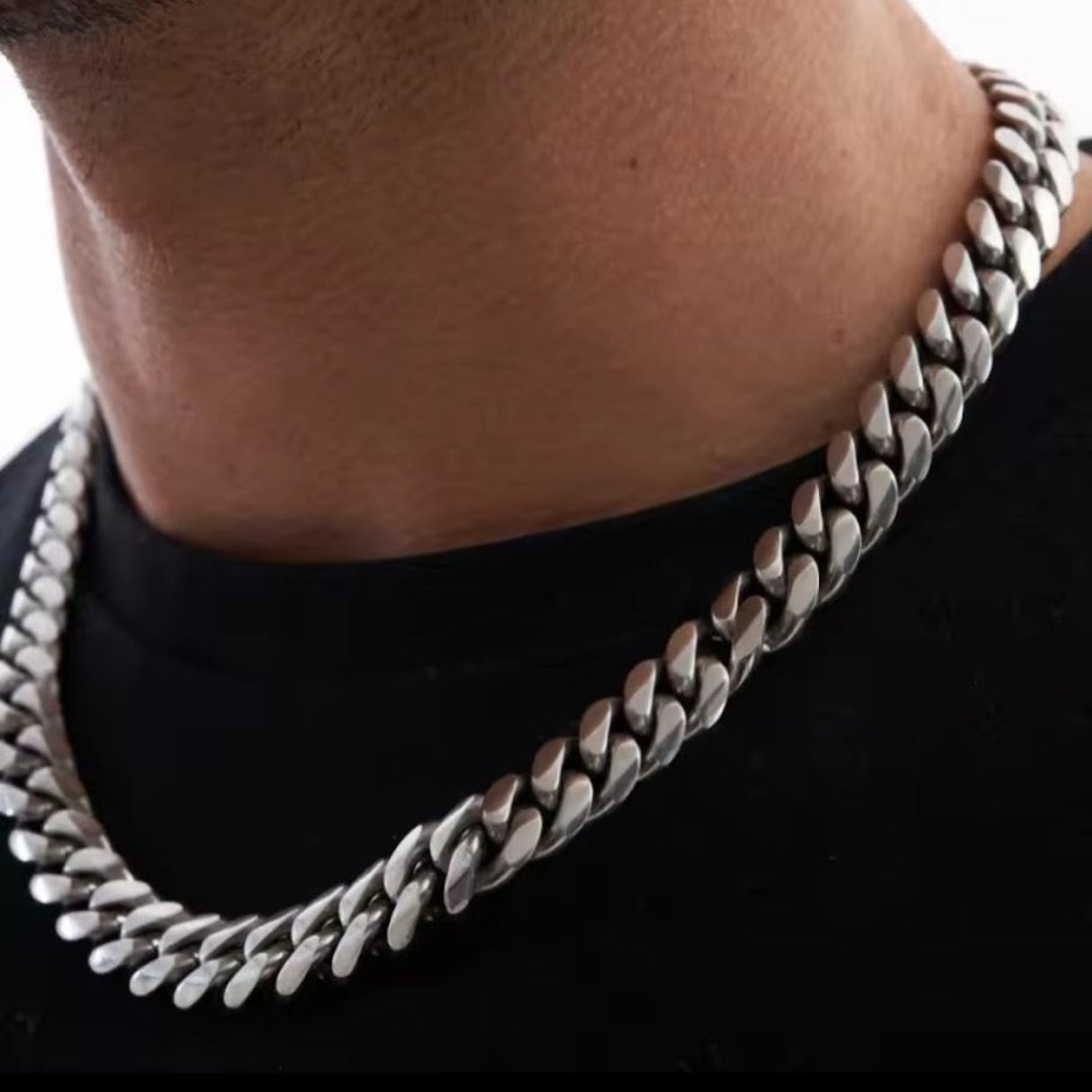 Close-up of a person wearing a silver chain necklace on a black background