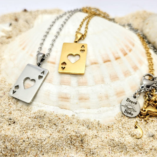 Two necklaces with heart-shaped pendants on a seashell with sand.