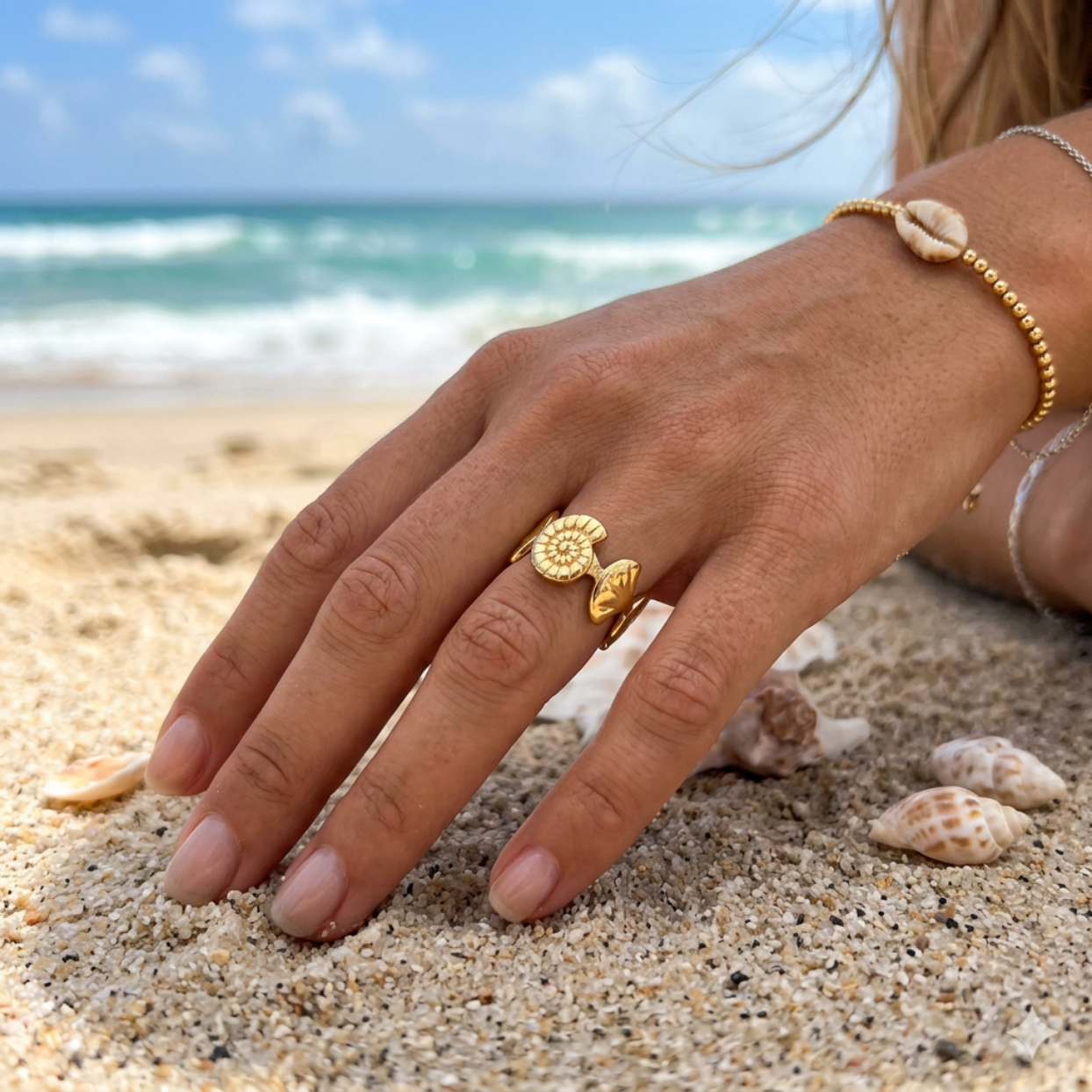 Hand with a gold ring on a sandy beach with ocean in the background