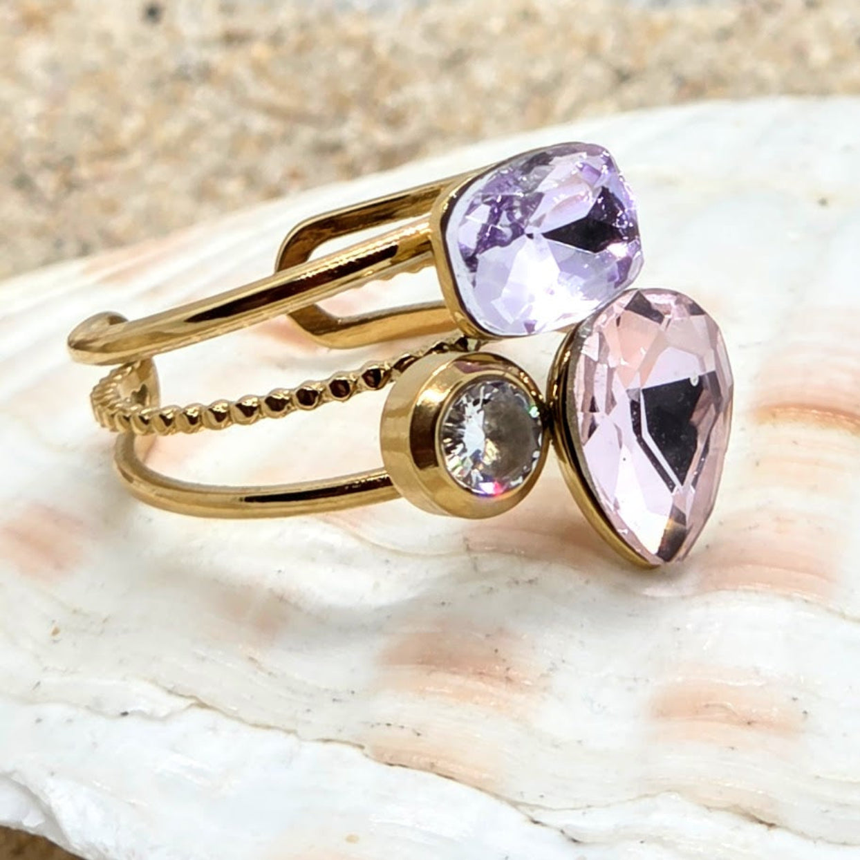 Gold ring with pink and clear gemstones on a shell background
