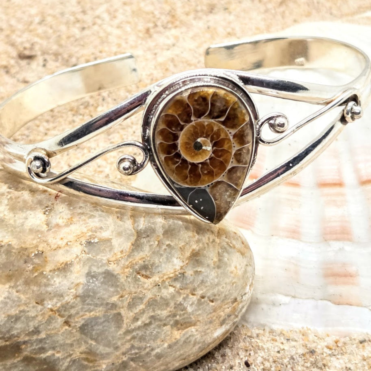 Silver bracelet with a central ammonite fossil on a stone surface