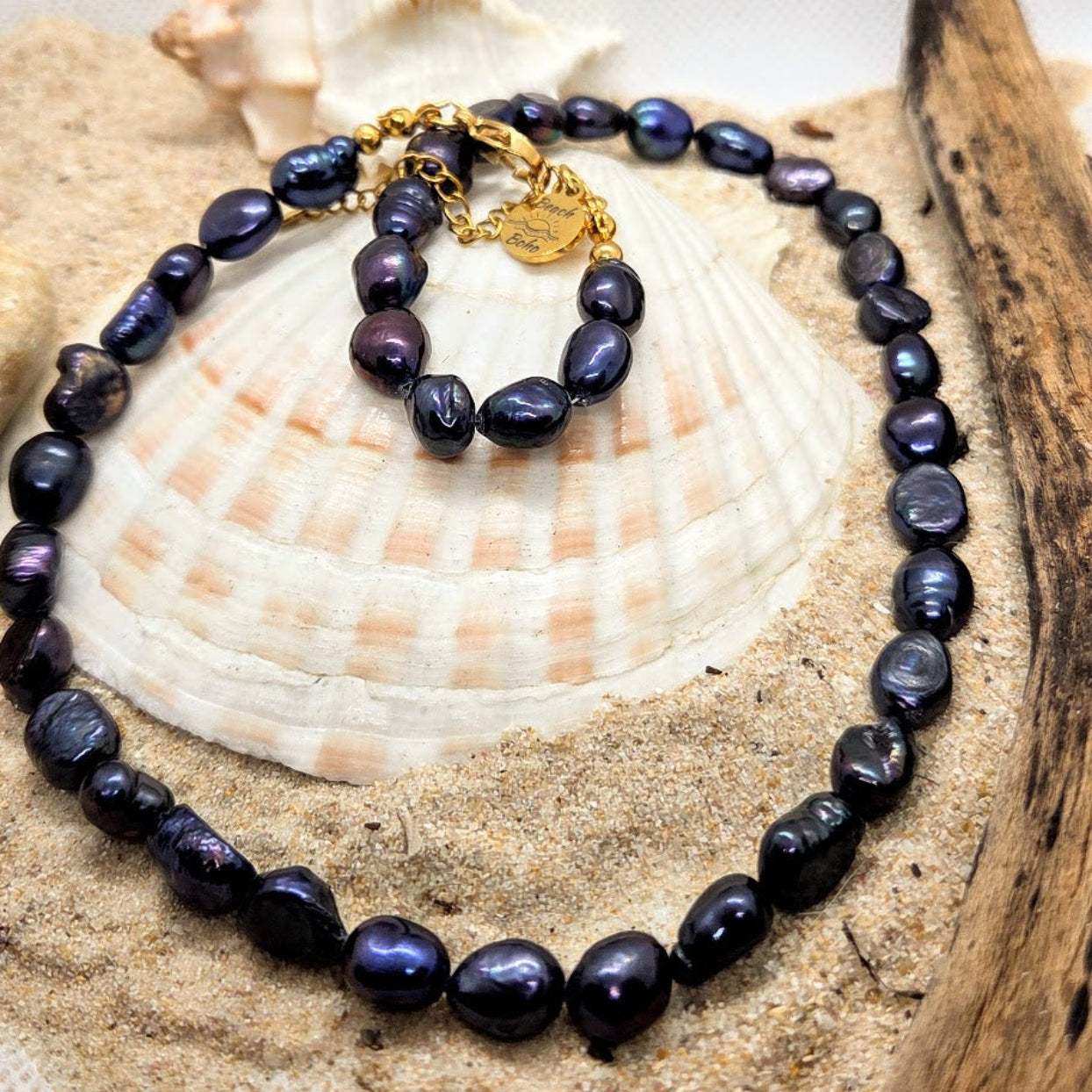 Black pearl necklace with a gold clasp on a shell and sand background