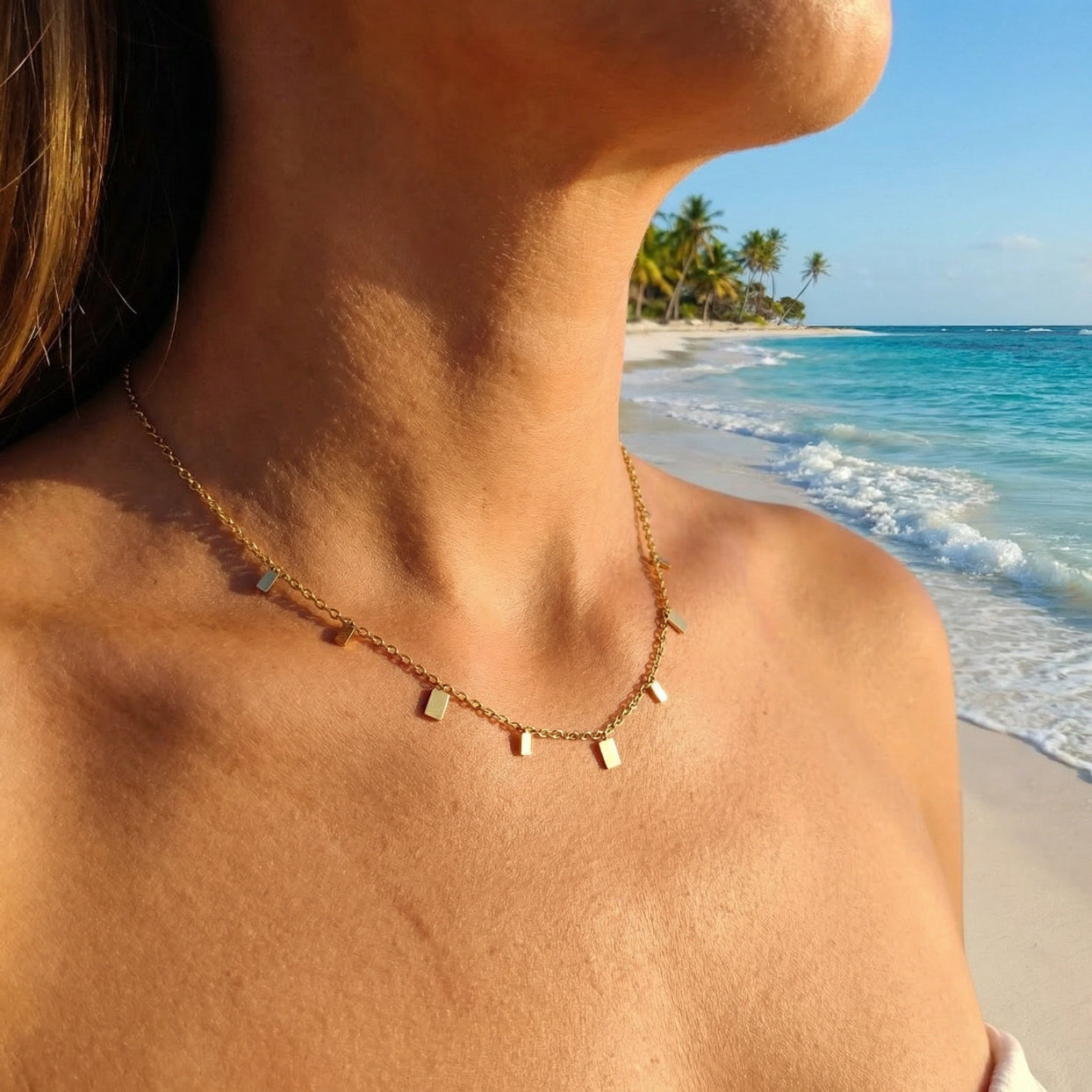 Necklace with small rectangular pendants worn by a person on a beach.