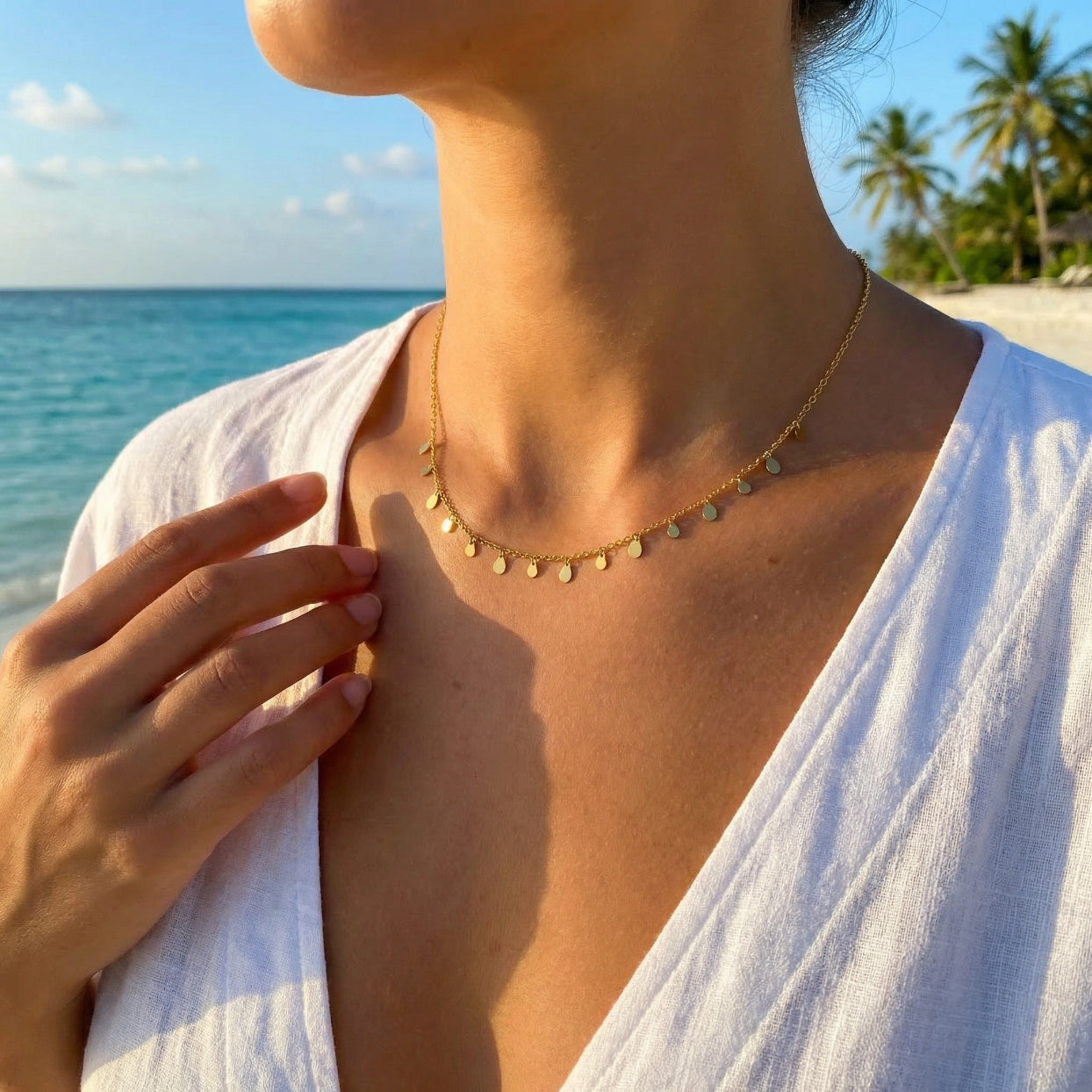 Person wearing a gold necklace with a beach and palm trees in the background