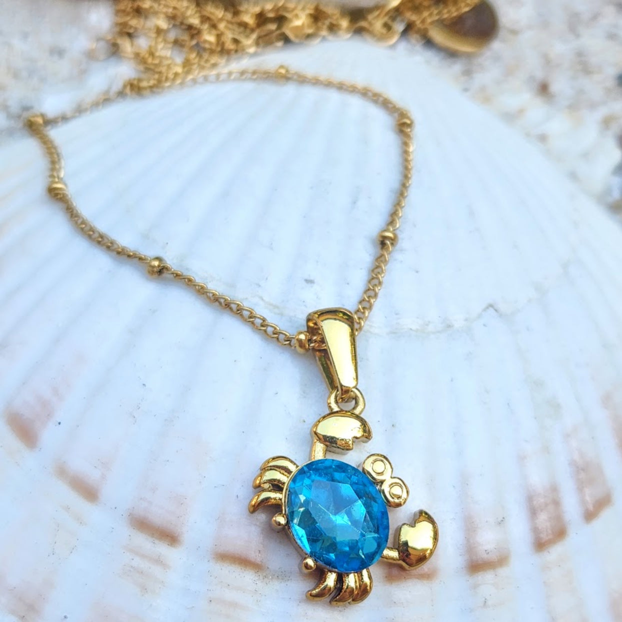 Gold crab-shaped necklace with a blue gemstone on a shell background
