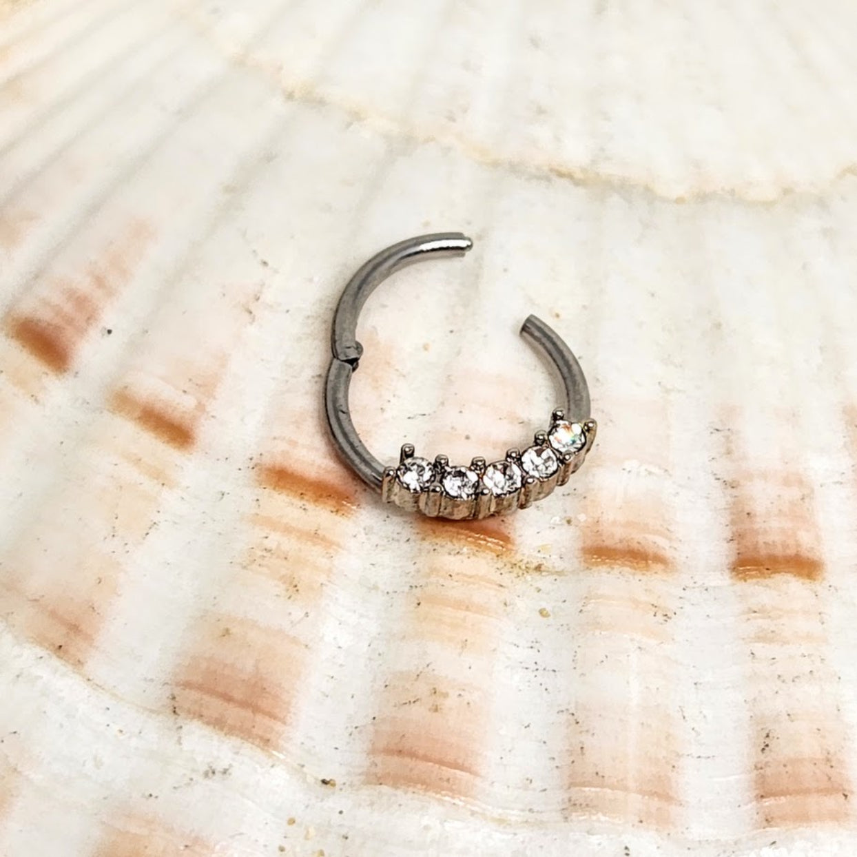 Silver septum ring with gemstones on a shell background