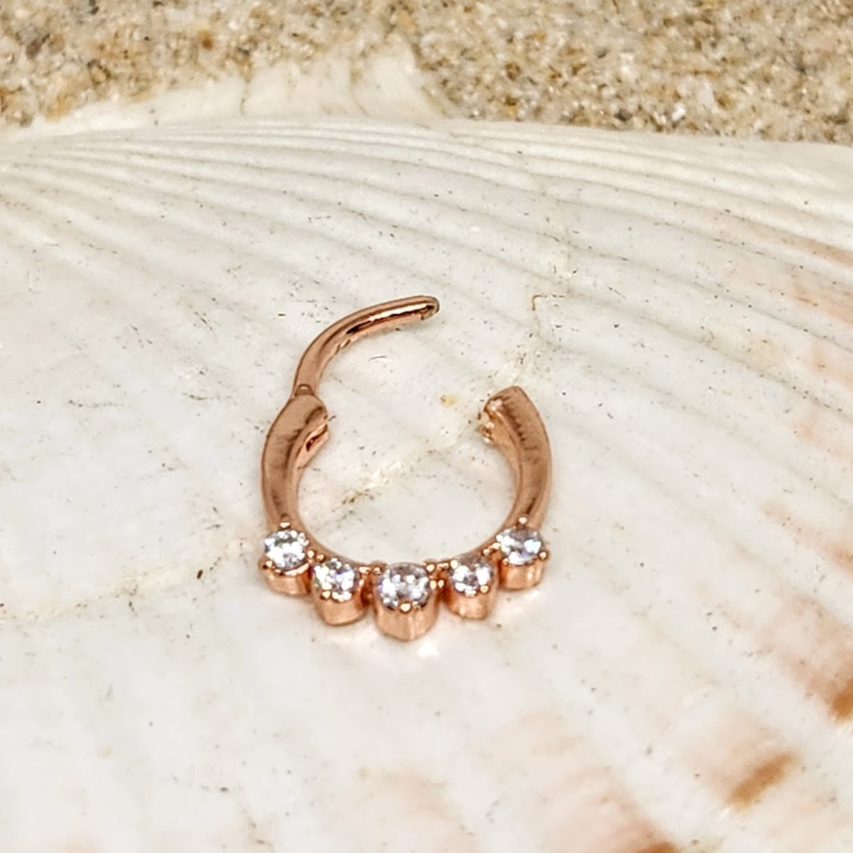 Rose gold hoop earring with three small diamonds on a shell background