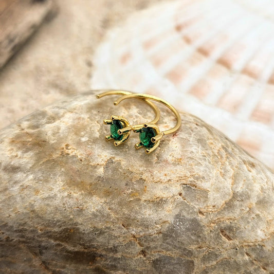 Gold hoop earrings with green gemstones on a stone surface