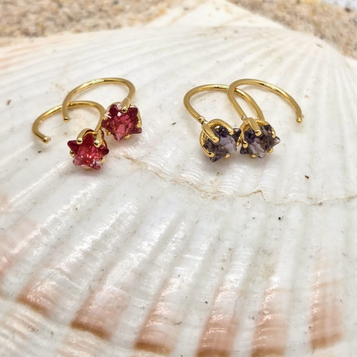 Gold earrings with red and purple gemstones on a shell
