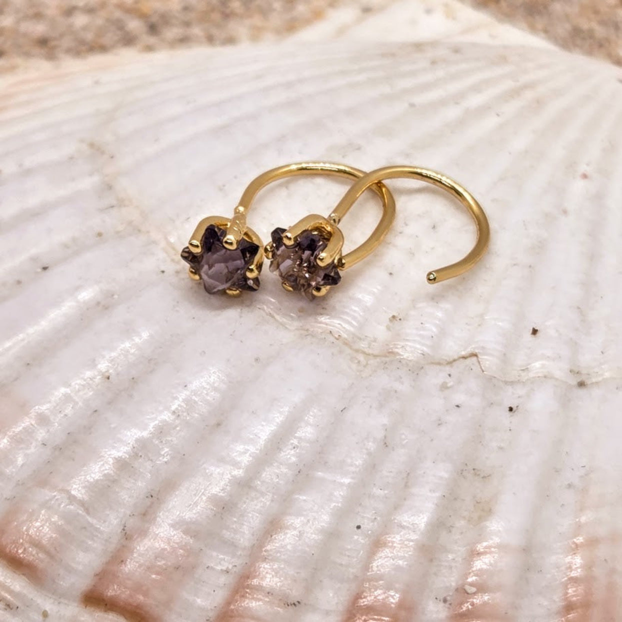 Gold earrings with smoky gemstones on a shell
