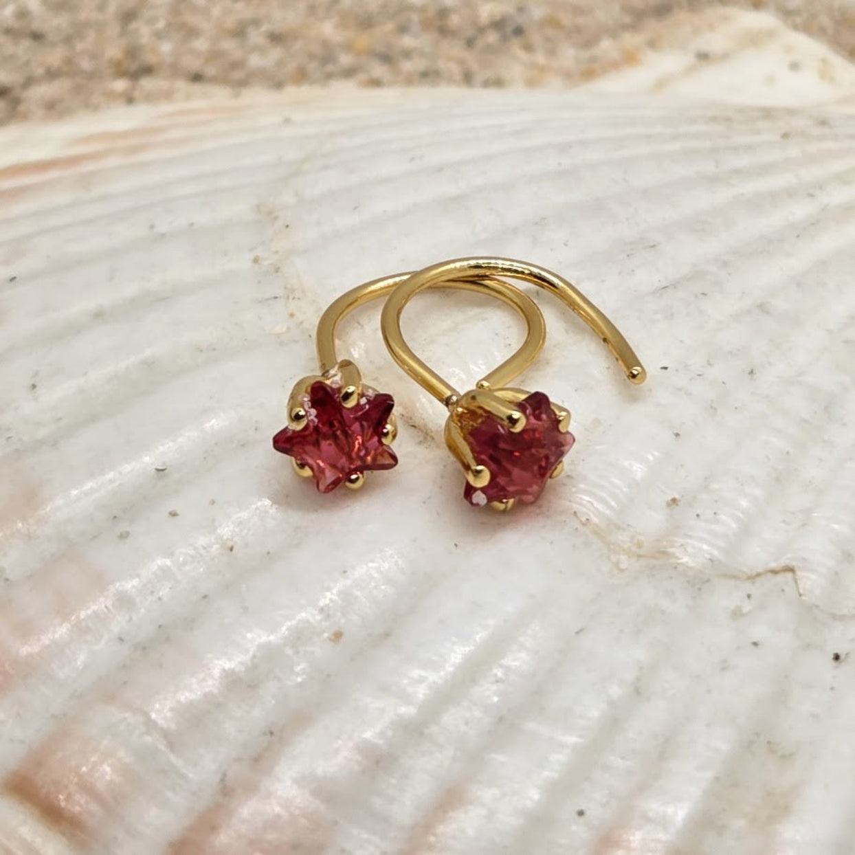 Gold earrings with red gemstones on a shell background