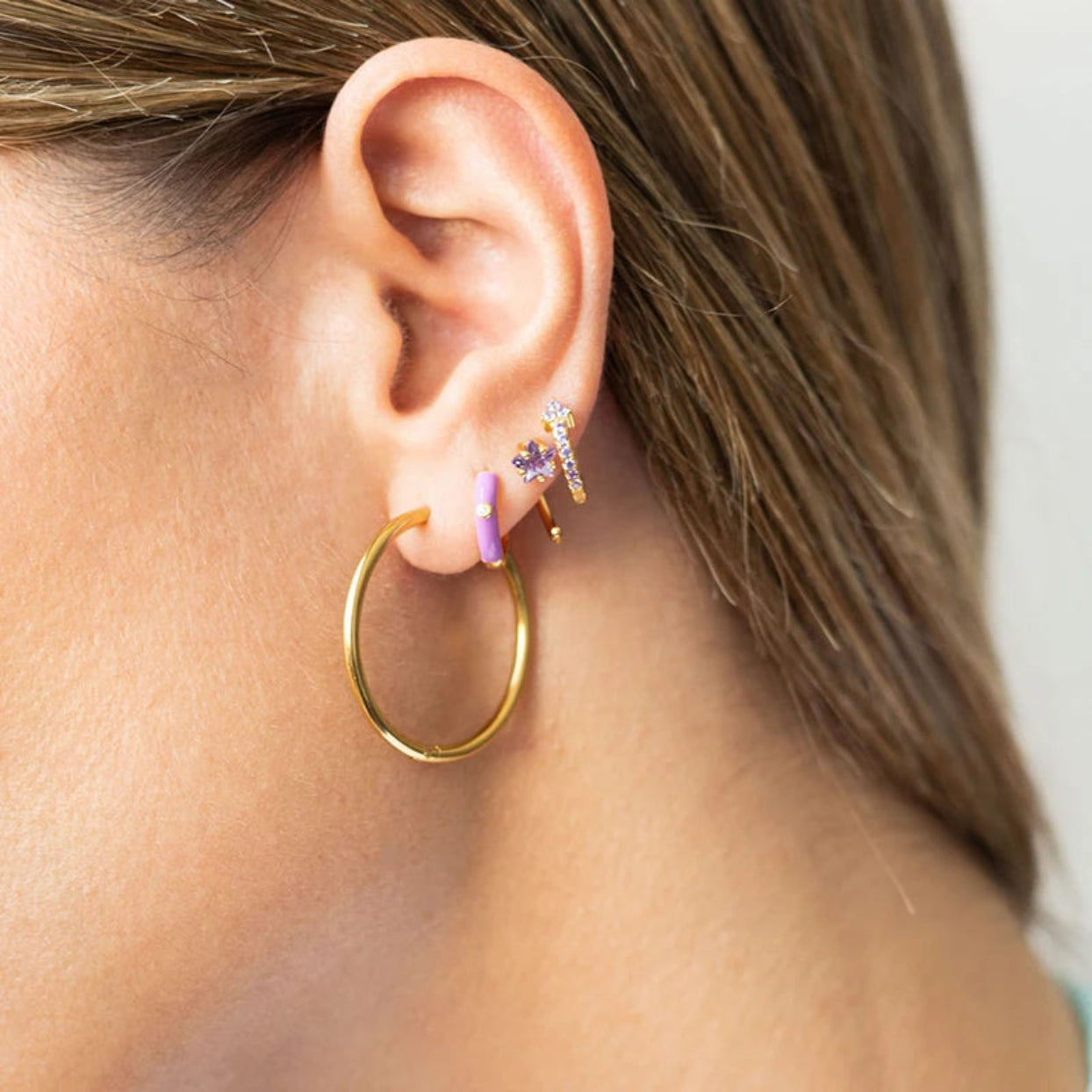 Close-up of an ear wearing gold hoop earrings with small accessories.