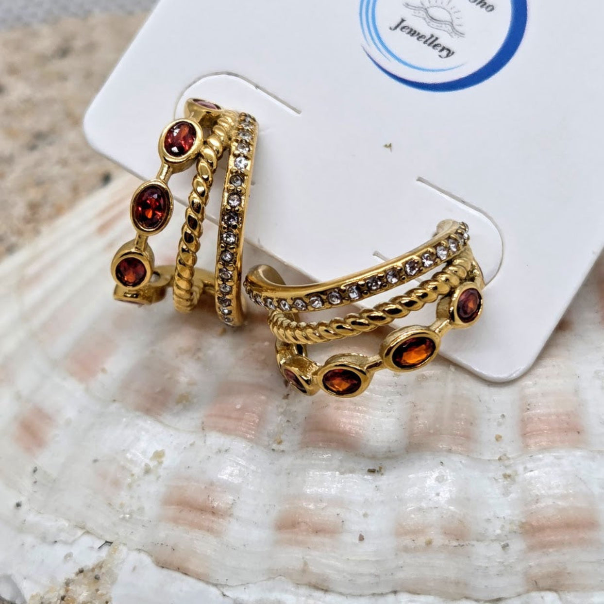Set of gold rings with red gemstones on a jewelry card, placed on a shell.