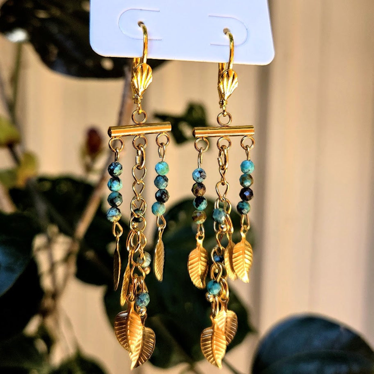 Pair of gold and blue beaded earrings on a display card with a blurred background