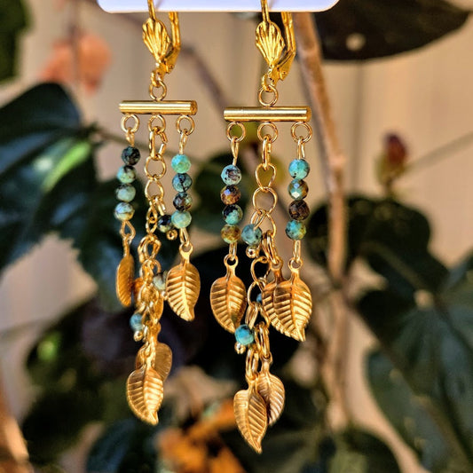 Gold leaf and bead earrings on a stand with a blurred plant background