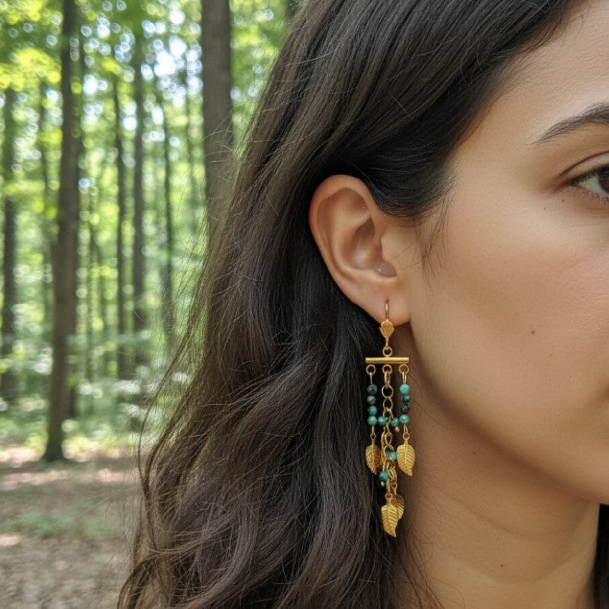 Close-up of a woman wearing gold earrings with green beads in a forest setting