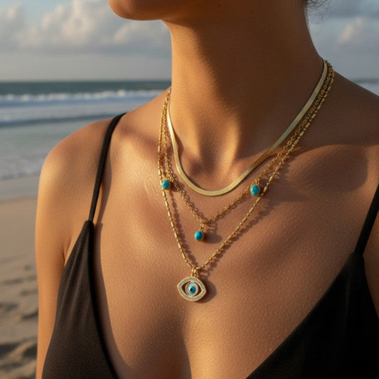 Person wearing a gold necklace with an eye pendant on a beach