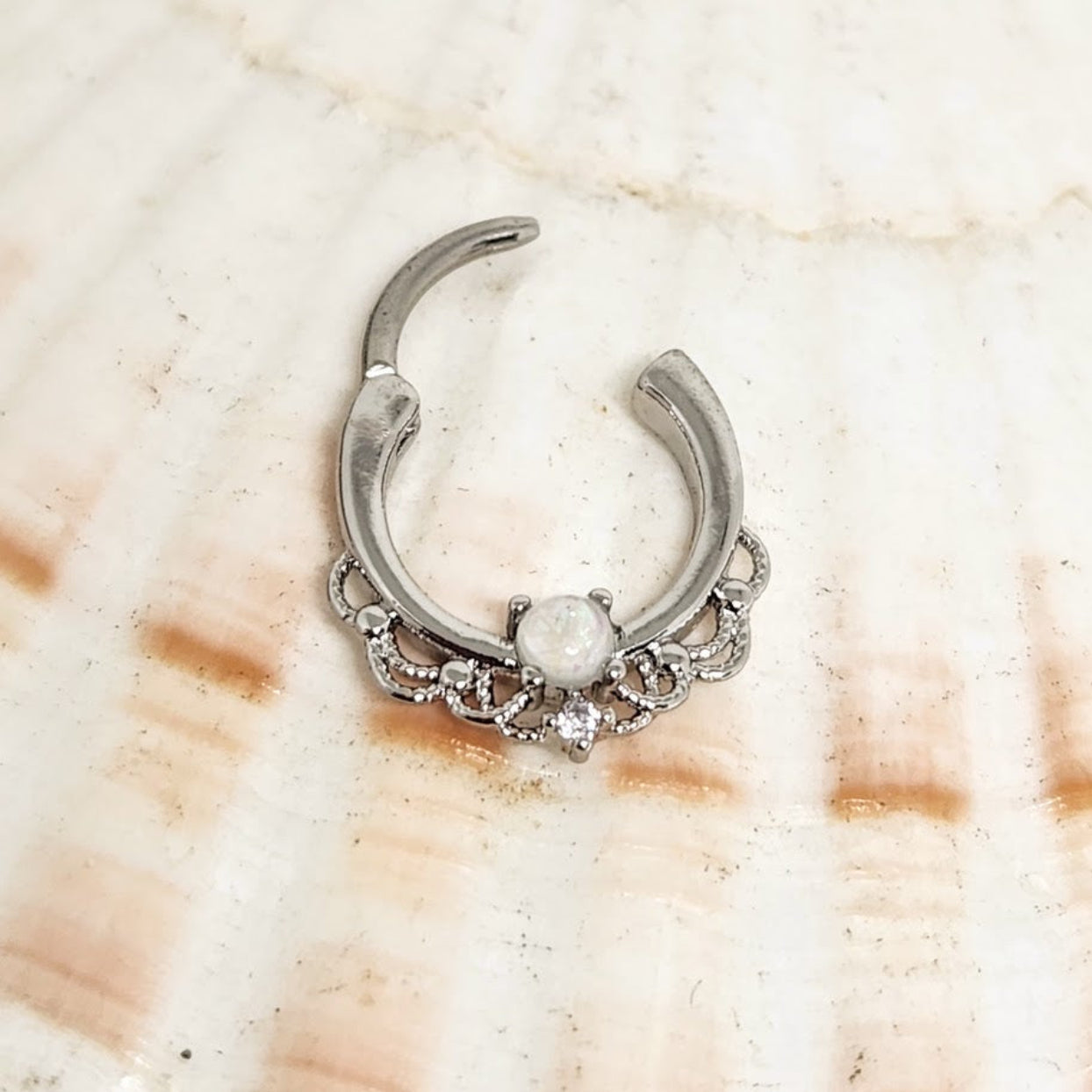 Silver nose ring with a central gemstone on a shell background
