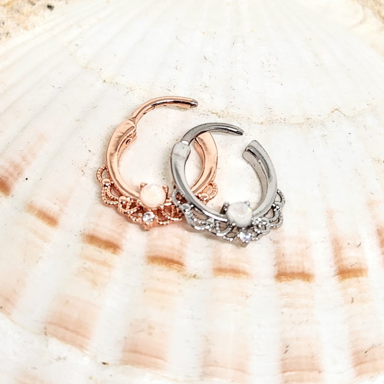 Two hoop earrings, one rose gold and one silver, on a seashell background.