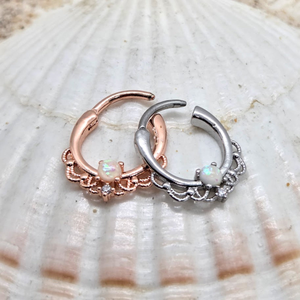Two hoop earrings, one rose gold and one silver, on a shell background.