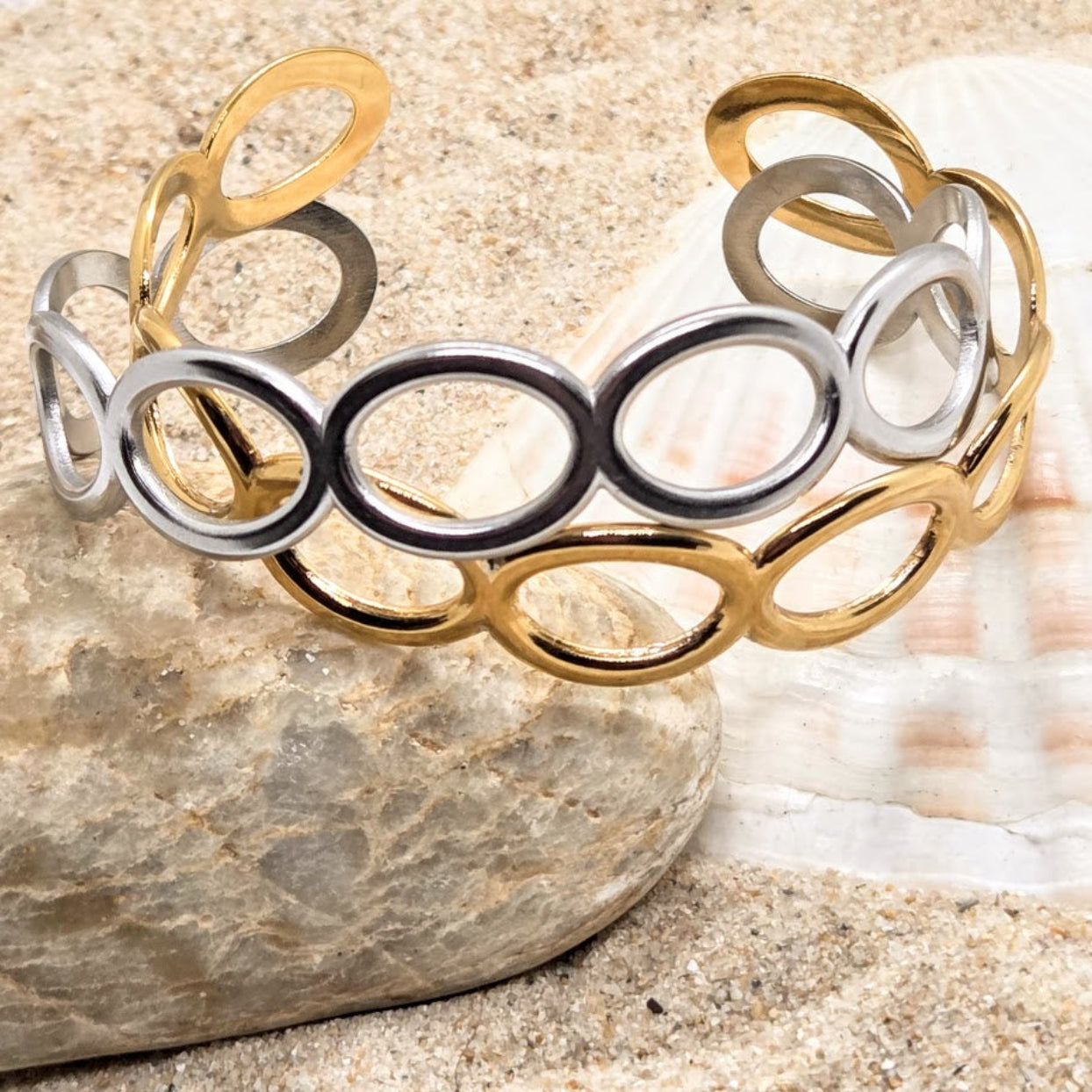 Gold and silver bracelet on a stone surface with a shell in the background