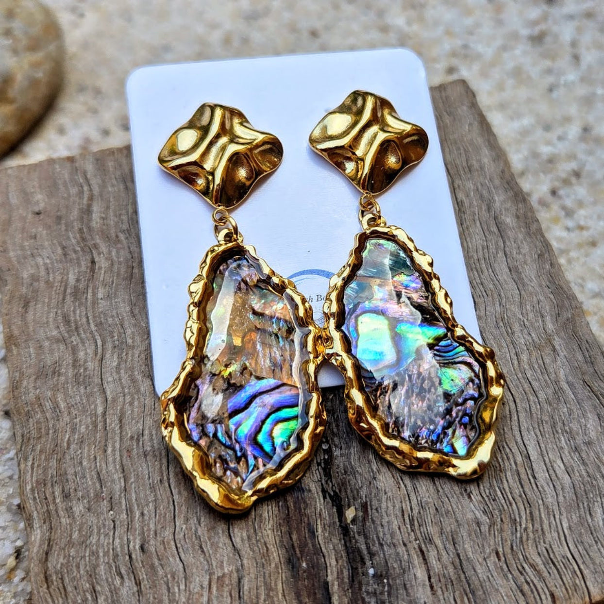 Gold-framed abalone shell earrings on a wooden surface