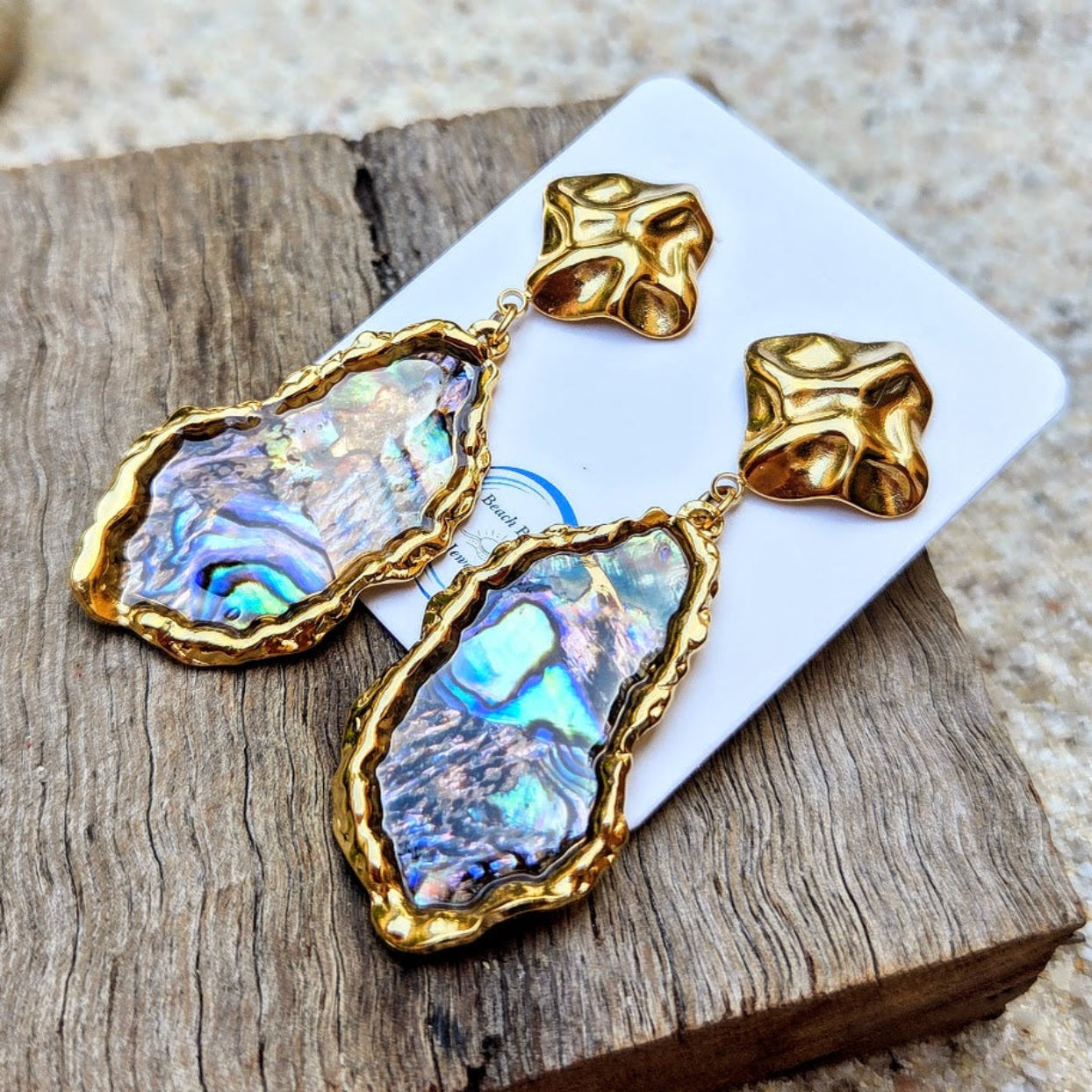 Gold and iridescent stone earrings on a wooden surface