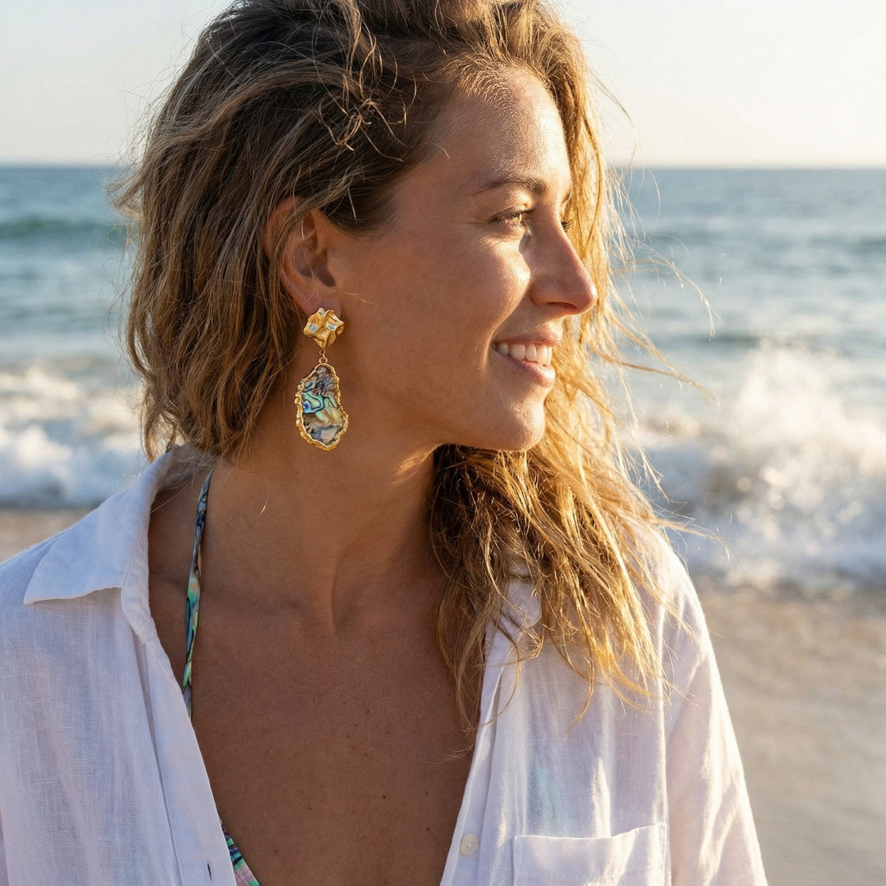 Woman on a beach wearing gold earrings with a blurred ocean background