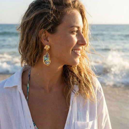 Woman on a beach wearing gold earrings with a blurred ocean background