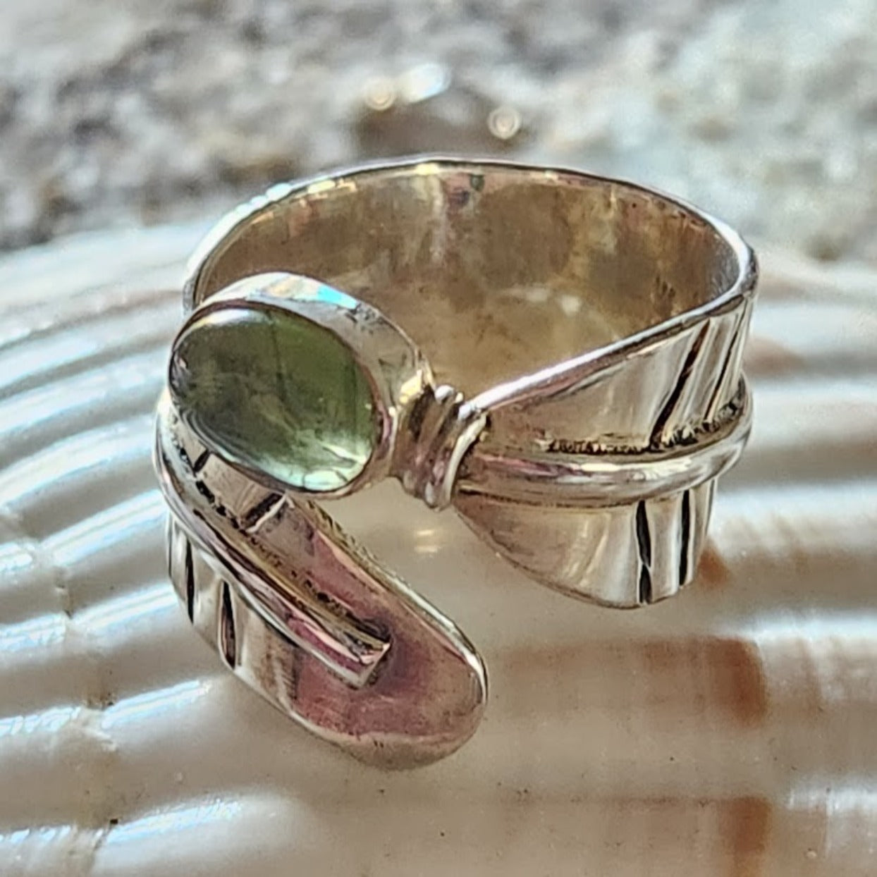 Silver ring with a green gemstone on a shell background