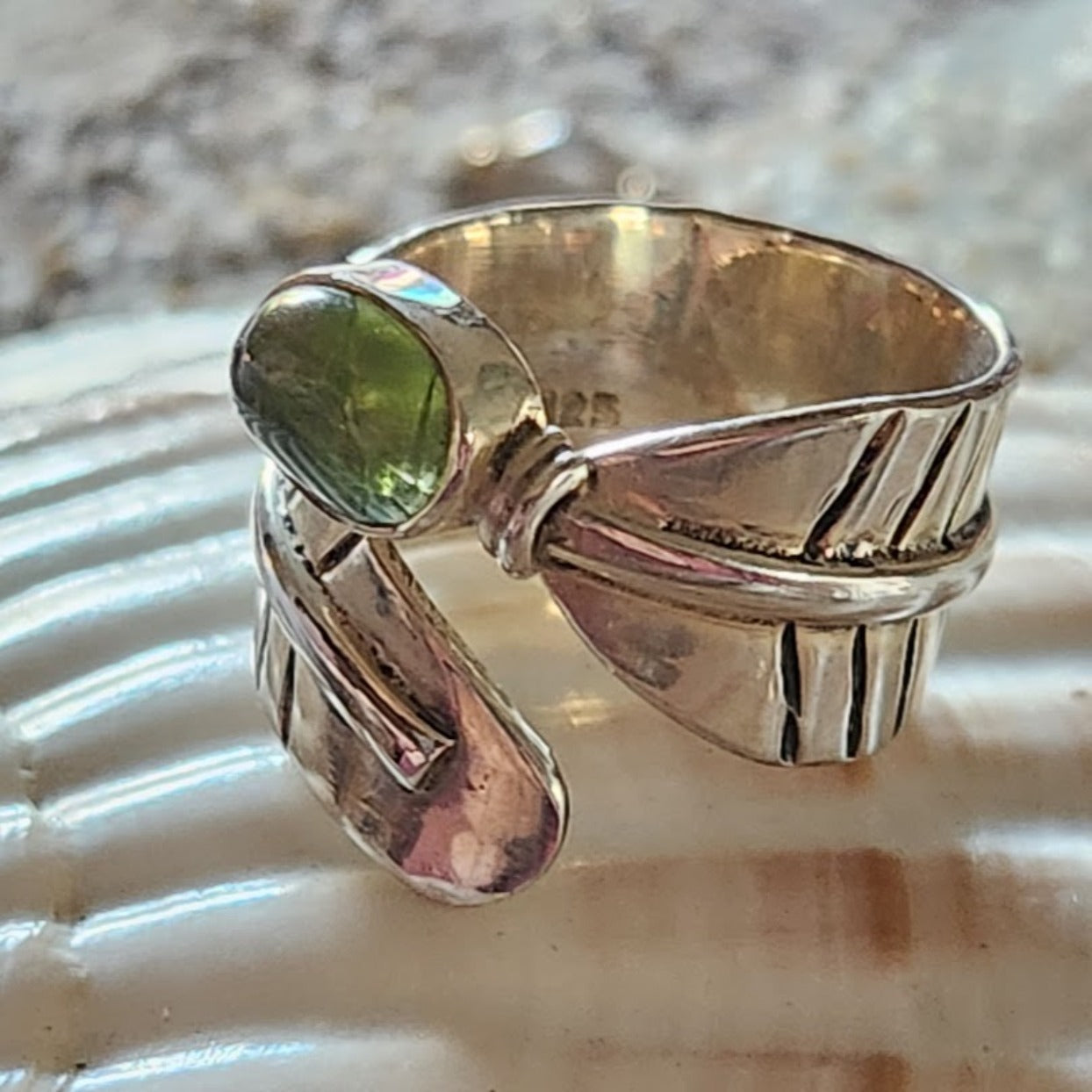 Silver ring with a green gemstone on a shell background