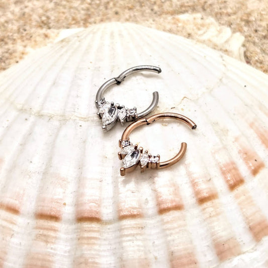 Two nose rings, one silver and one rose gold, on a seashell.