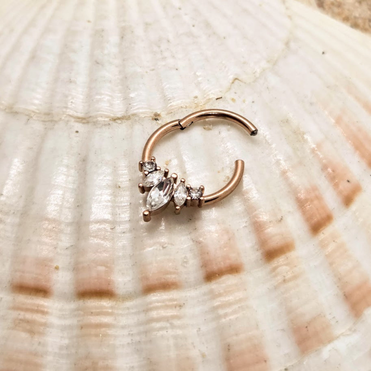 Rose gold nose ring with marquise-shaped gemstones on a shell background