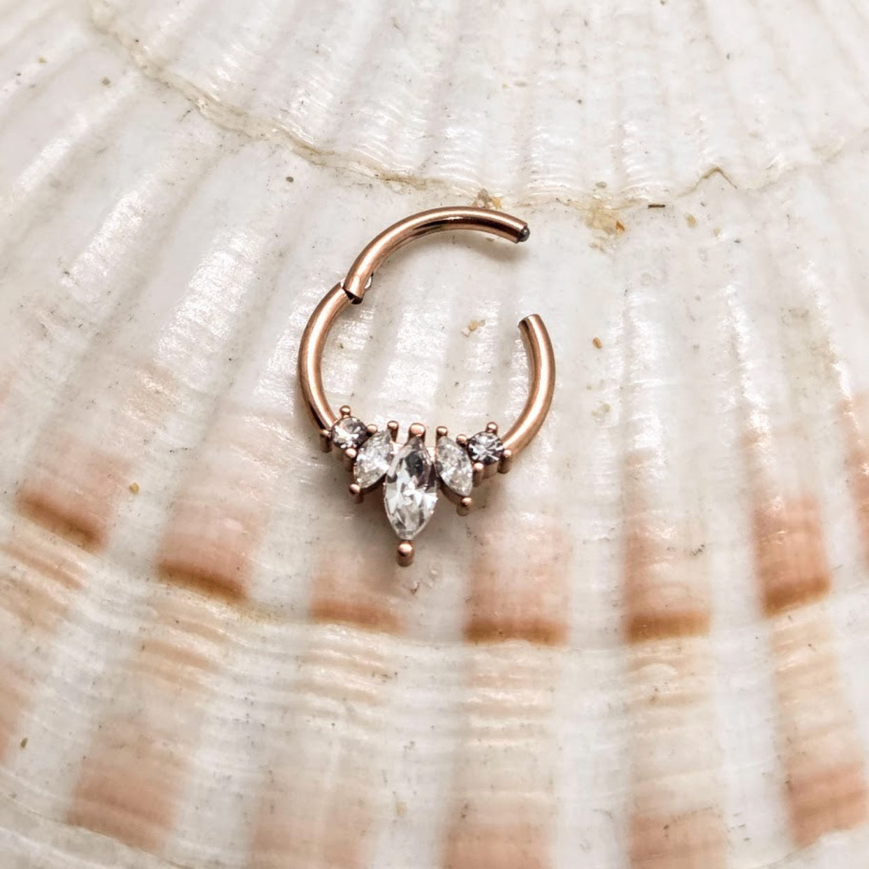 Rose gold hoop earring with marquise-shaped gemstones on a shell background
